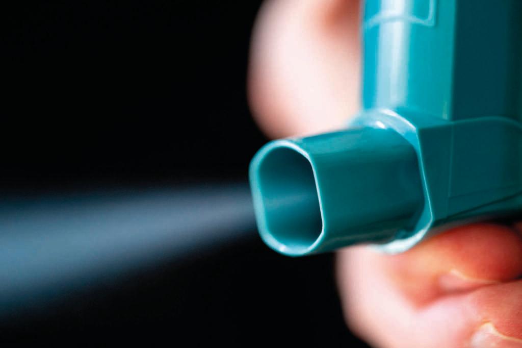 Hand mit blauem Asthma-Inhalator mit Spray auf schwarzem Hintergrund.