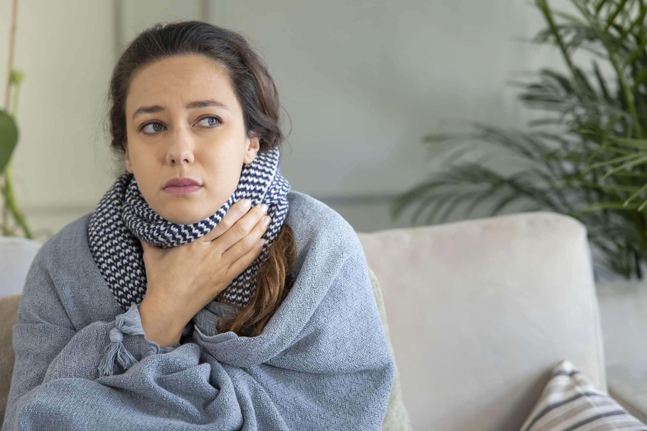 Junge Frau berührt schmerzhaften Hals, Halsschmerzen bei Grippe, Erkältung und Infektion