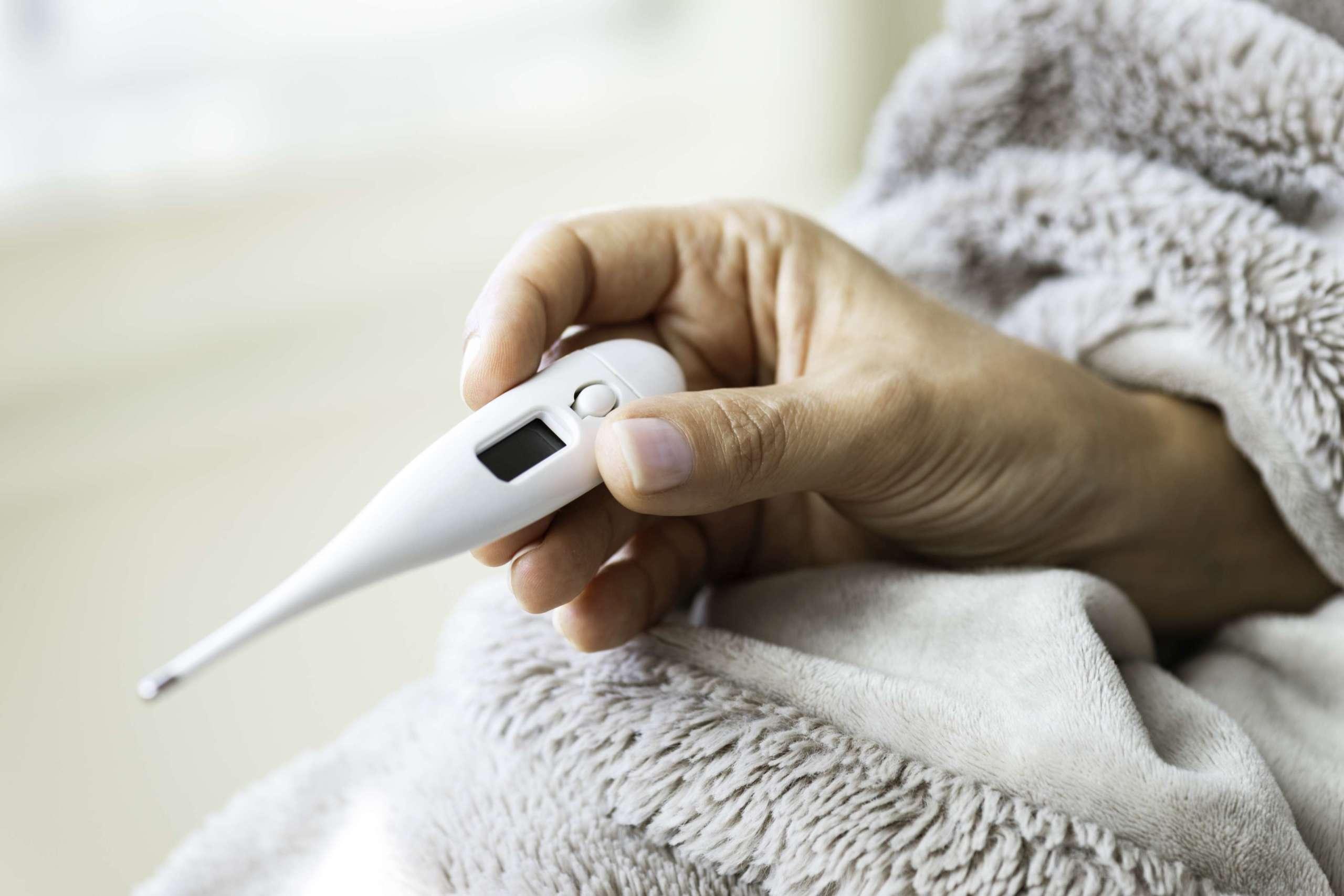 Unerkennbare weibliche Hand in weißer Decke hält Thermometer in der Hand und überprüft ihr Fieber.