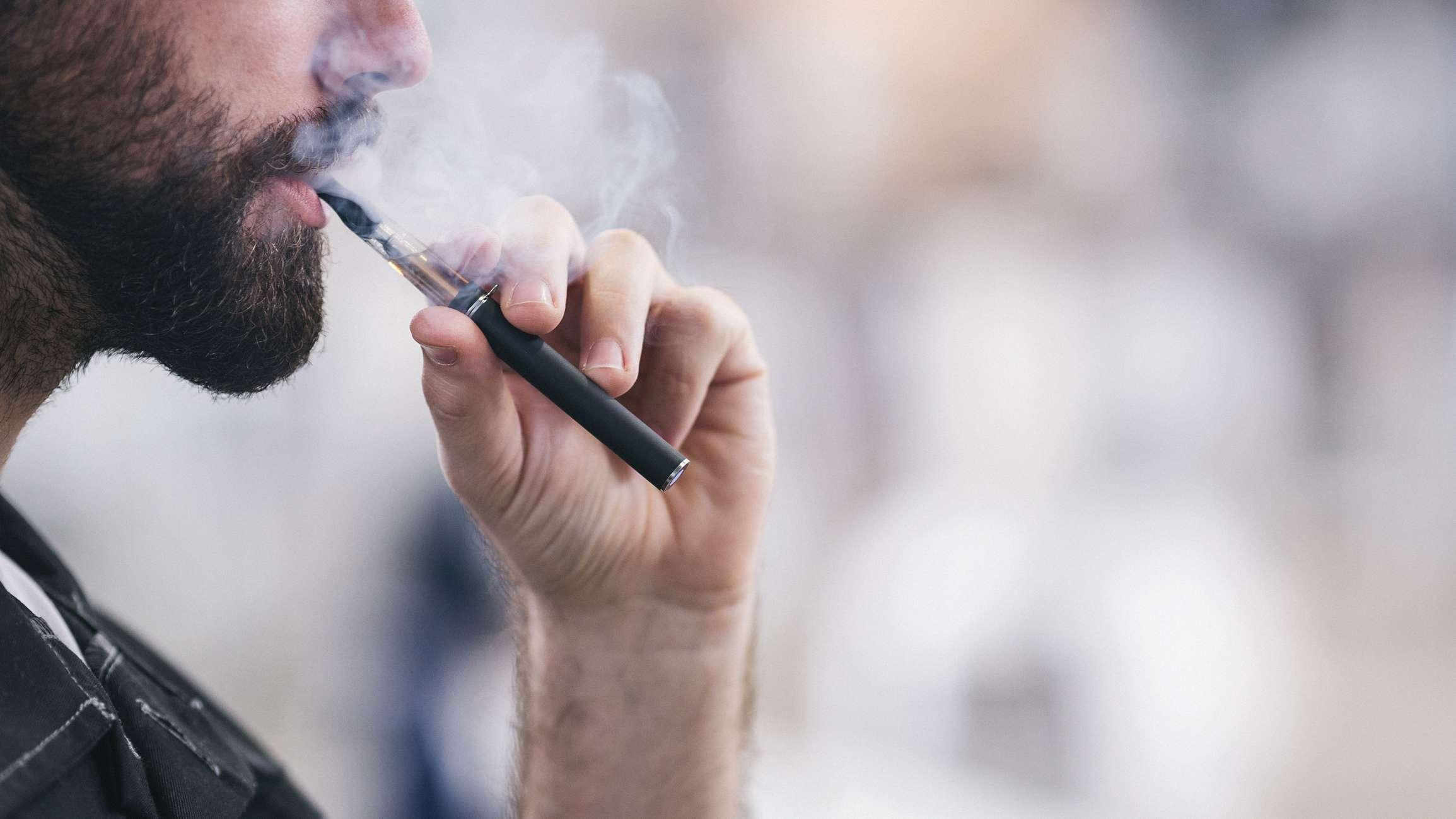 Junger männlicher Arbeiter, der elektronische Zigarette raucht