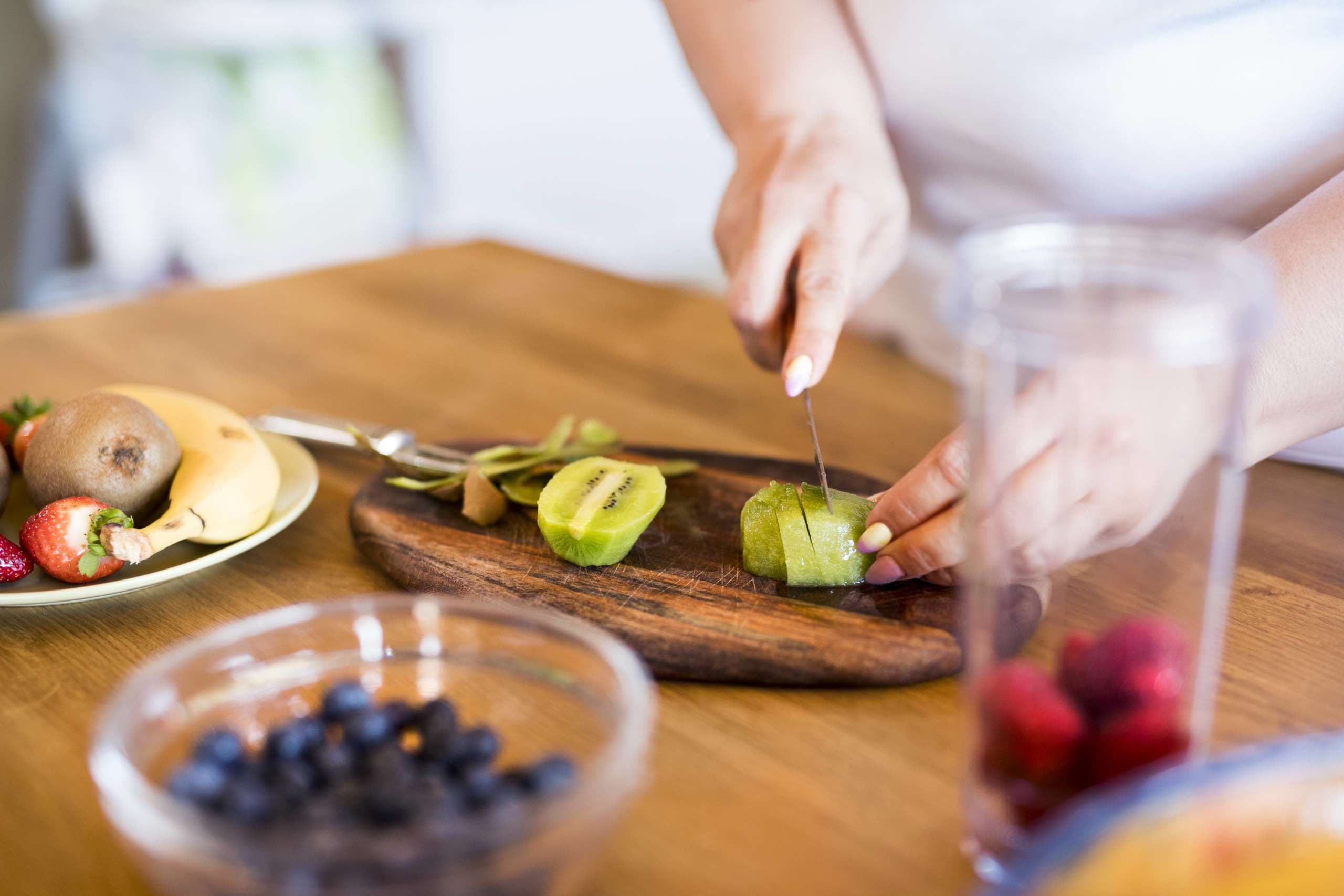 Nicht erkennbare übergewichtige Frau in weißem T-Shirt zu Hause, die in ihrer Küche einen köstlichen, gesunden Smoothie zubereitet.