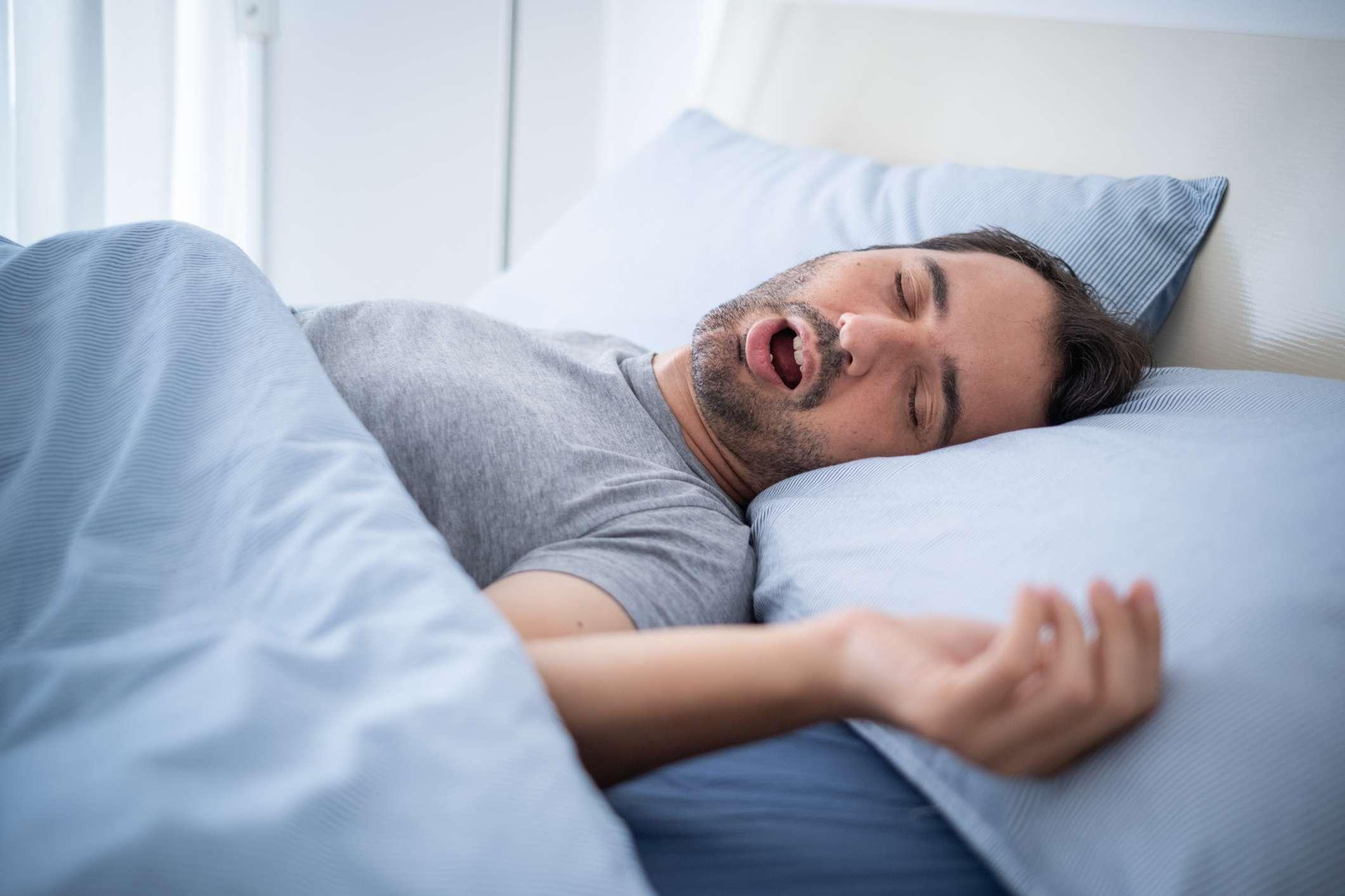 Mann schnarcht laut in seinem Bett, während er schläft