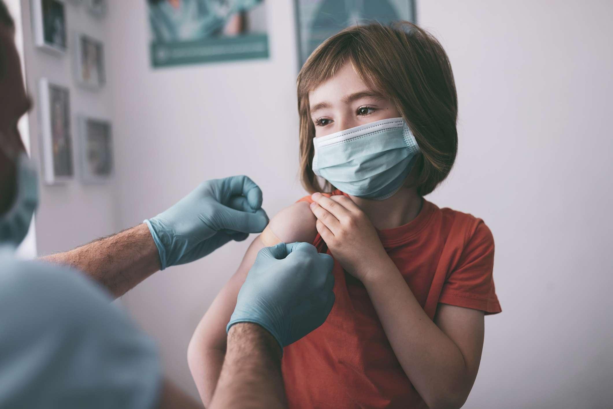 Arzt legt einem Kind nach der Injektion des Covid-19-Impfstoffs einen Klebeverband an.