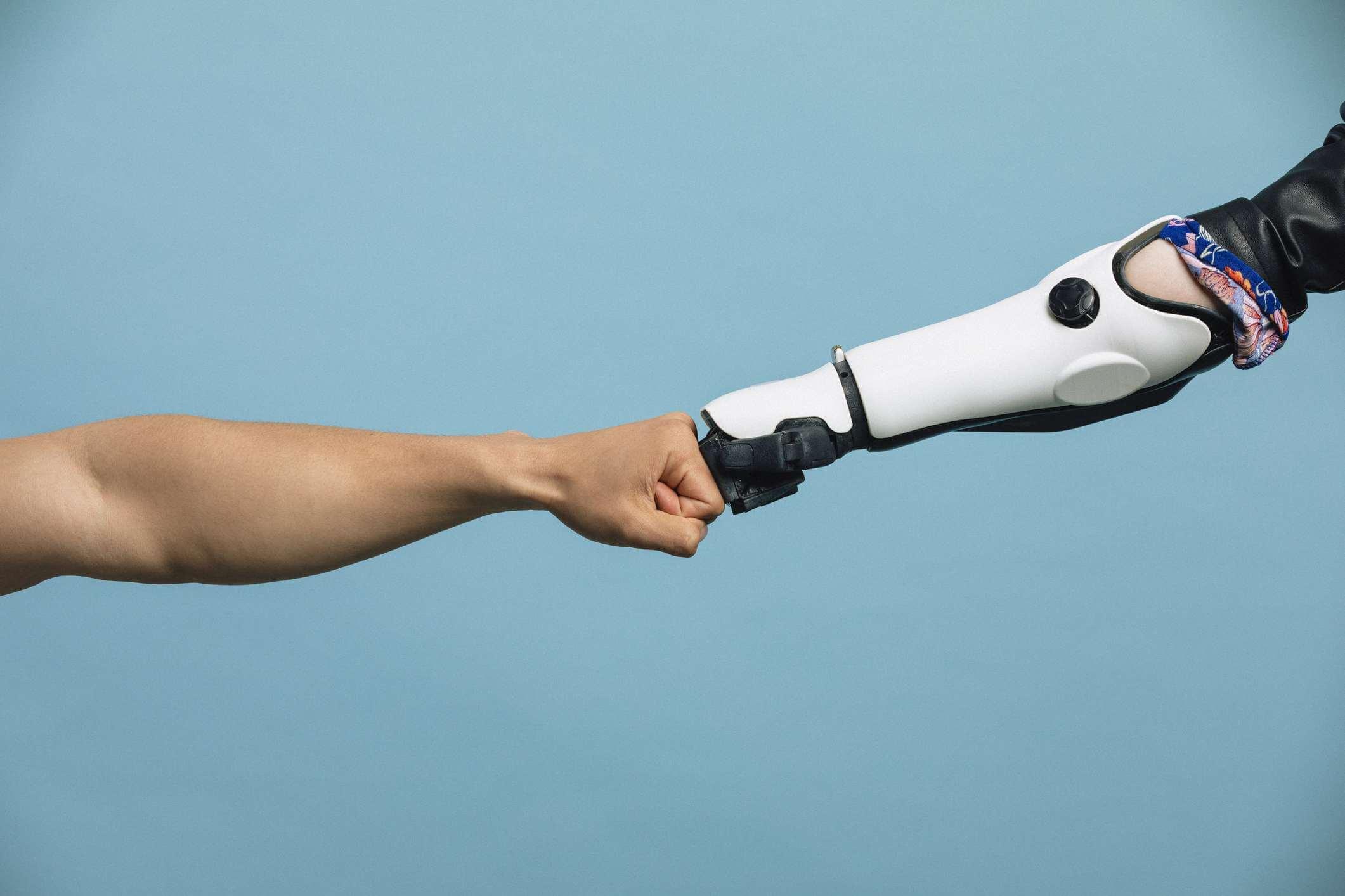 Eine menschliche Hand und eine Roboterhand treffen sich in der Mitte und berühren die Knöchel.