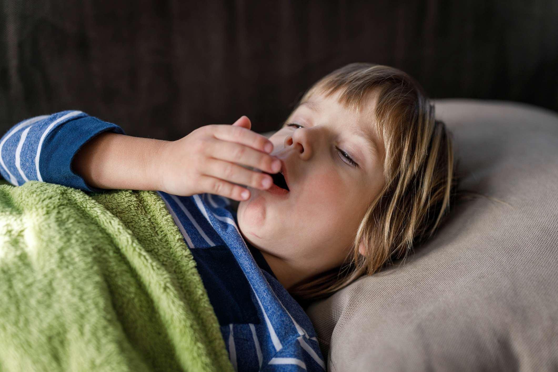 Kleiner kranker Junge hustet, während er zu Hause einen Virus im Bett hat.