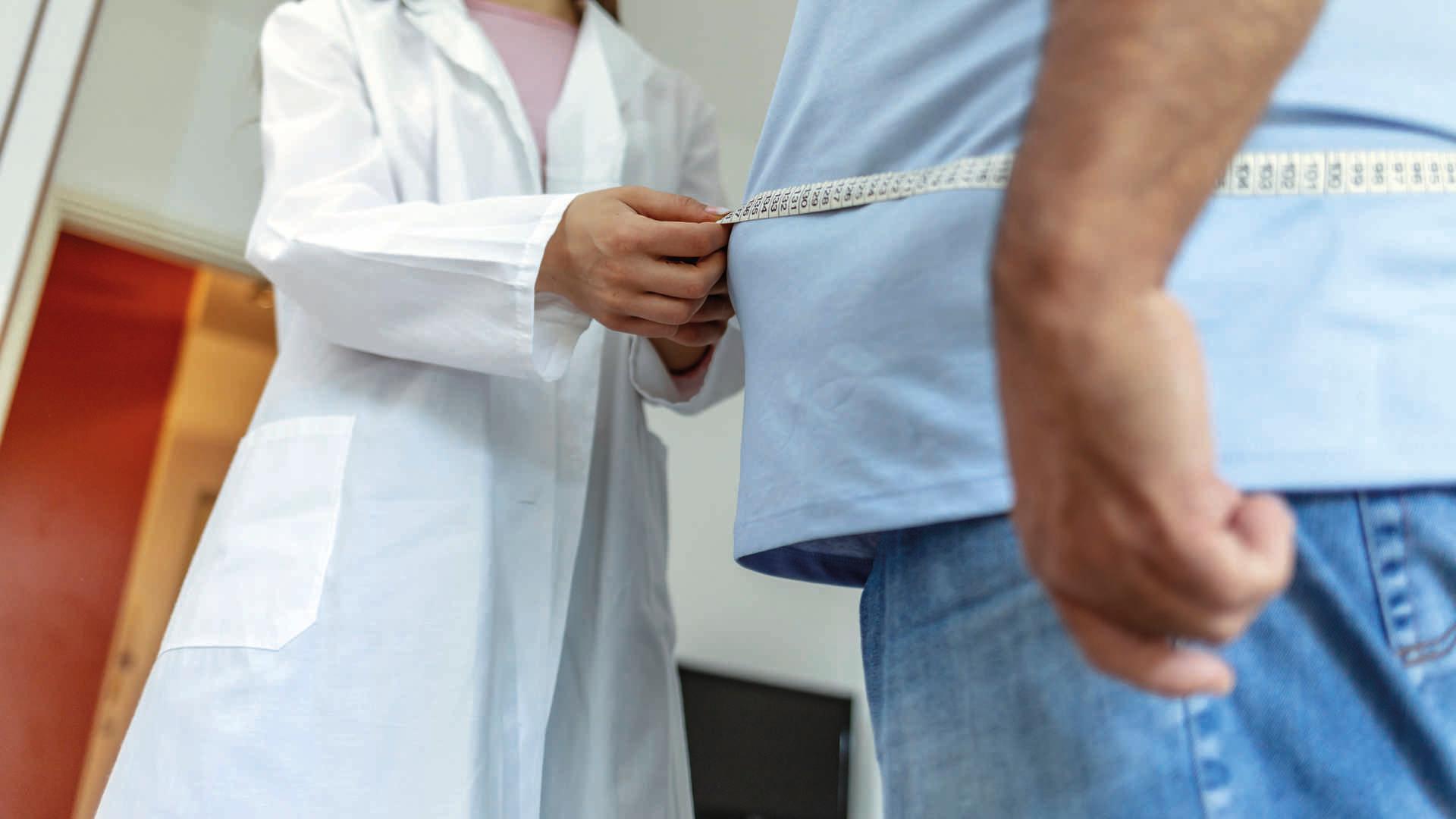 Ein Ernährungsarzt misst den Körper eines männlichen Patienten mit einem Maßband auf Fettgewebe und Übergewicht.