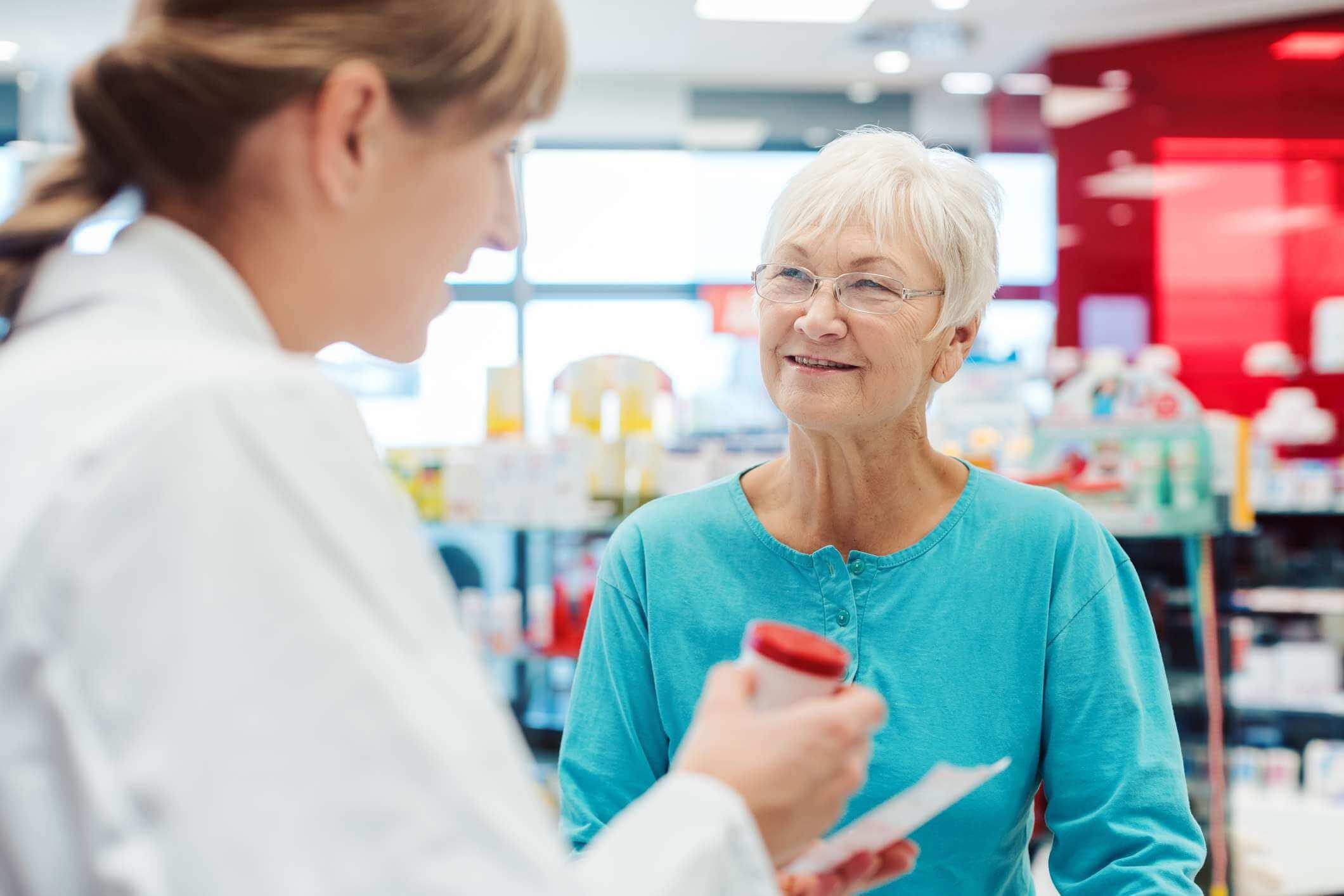 Ältere Frau in der Apotheke, die mit dem Chemiker oder Apotheker spricht, erklärt die Wirkung eines Medikaments