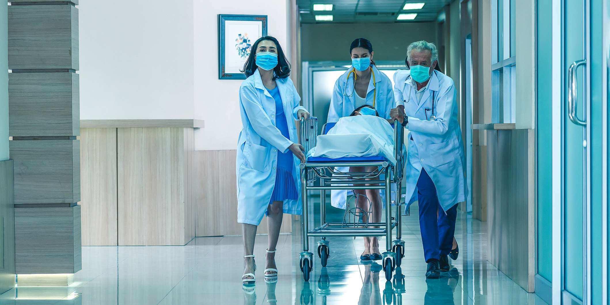 Rückansicht der Ärzte, die zur Operation rennen. Krankenhaus-Notfallteam, das eine Trage mit Patient durch die Krankenhaushalle trägt.