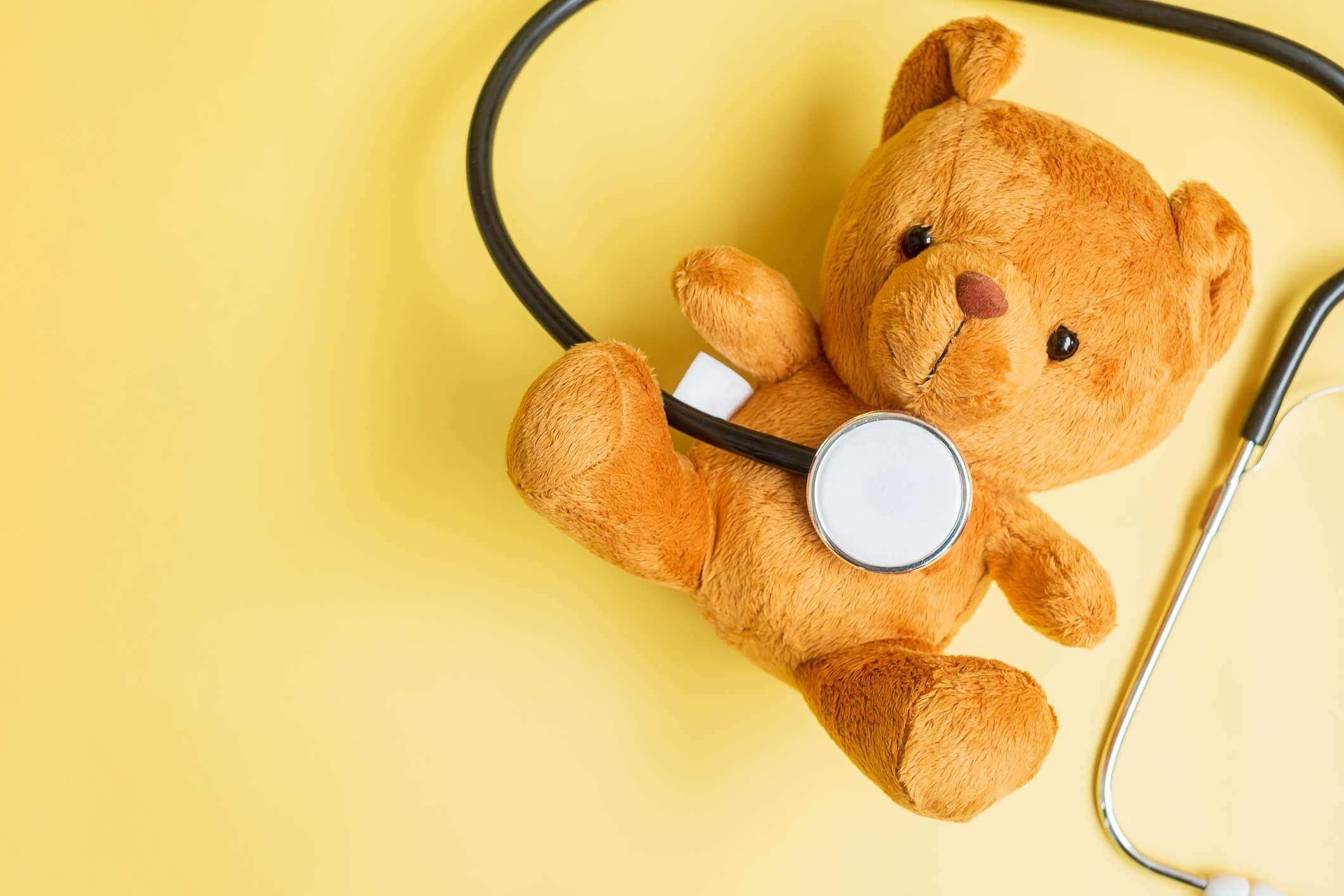 Stethoskop mit Bärenpuppe auf gelbem Hintergrund zur Unterstützung des Lebens und der Krankheit von Kindern. September Childhood Cancer Awareness Month, Gesundheits- und Lebensversicherungskonzept