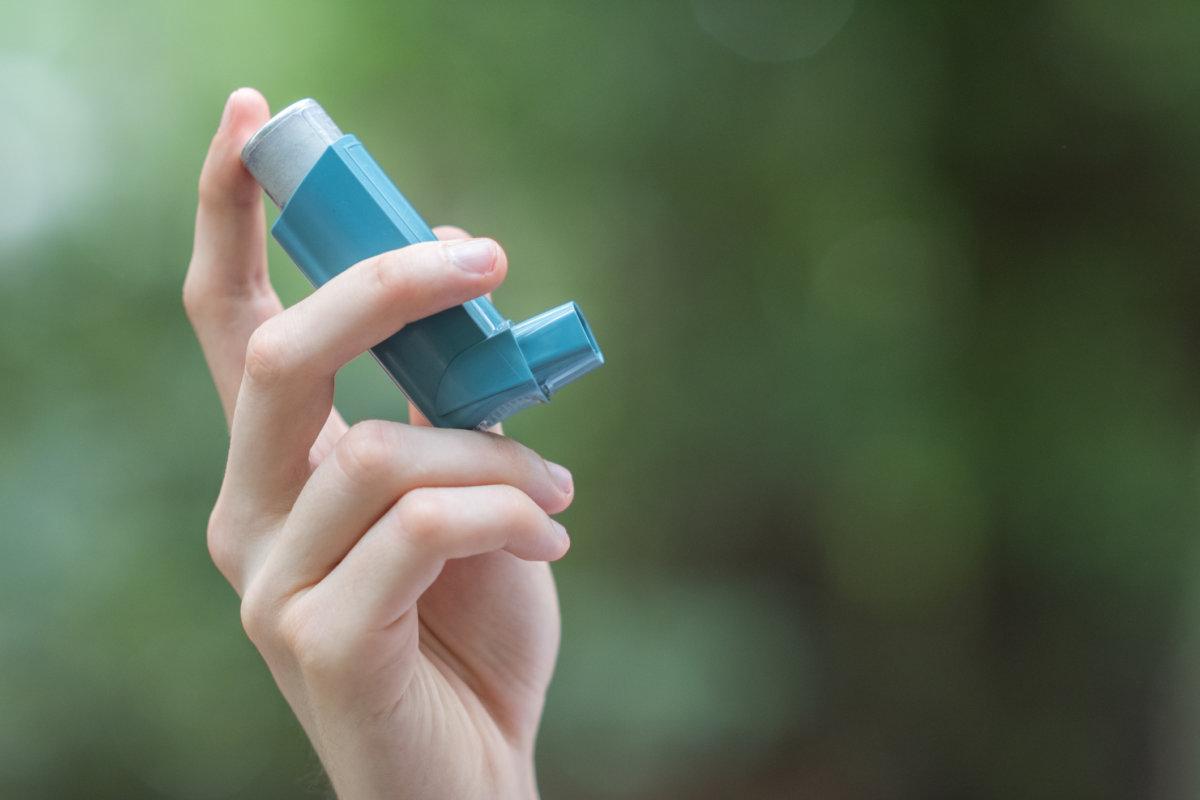 Blick auf die Hand eines Mannes, der einen blauen Asthmainhalator hält