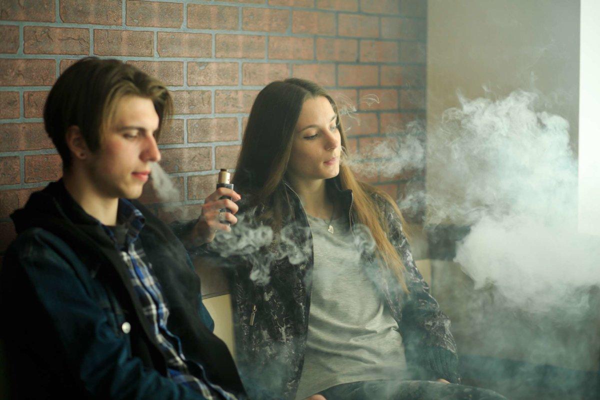Vape-Teenager. Junges süßes Mädchen mit Sonnenbrille und junger gutaussehender Mann rauchen elektronische Zigaretten in der Vape-Bar. Schlechte Angewohnheit, die der Gesundheit schadet.