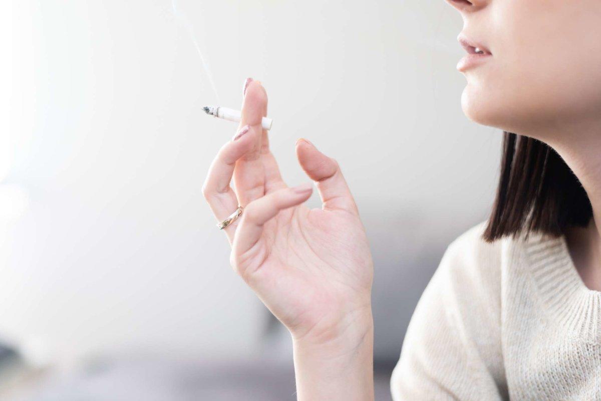 Junges, ungesundes Millennial-Mädchen, das auf einer Couch in ihrer Wohnung eine Zigarette raucht, Seitenansicht, Profil