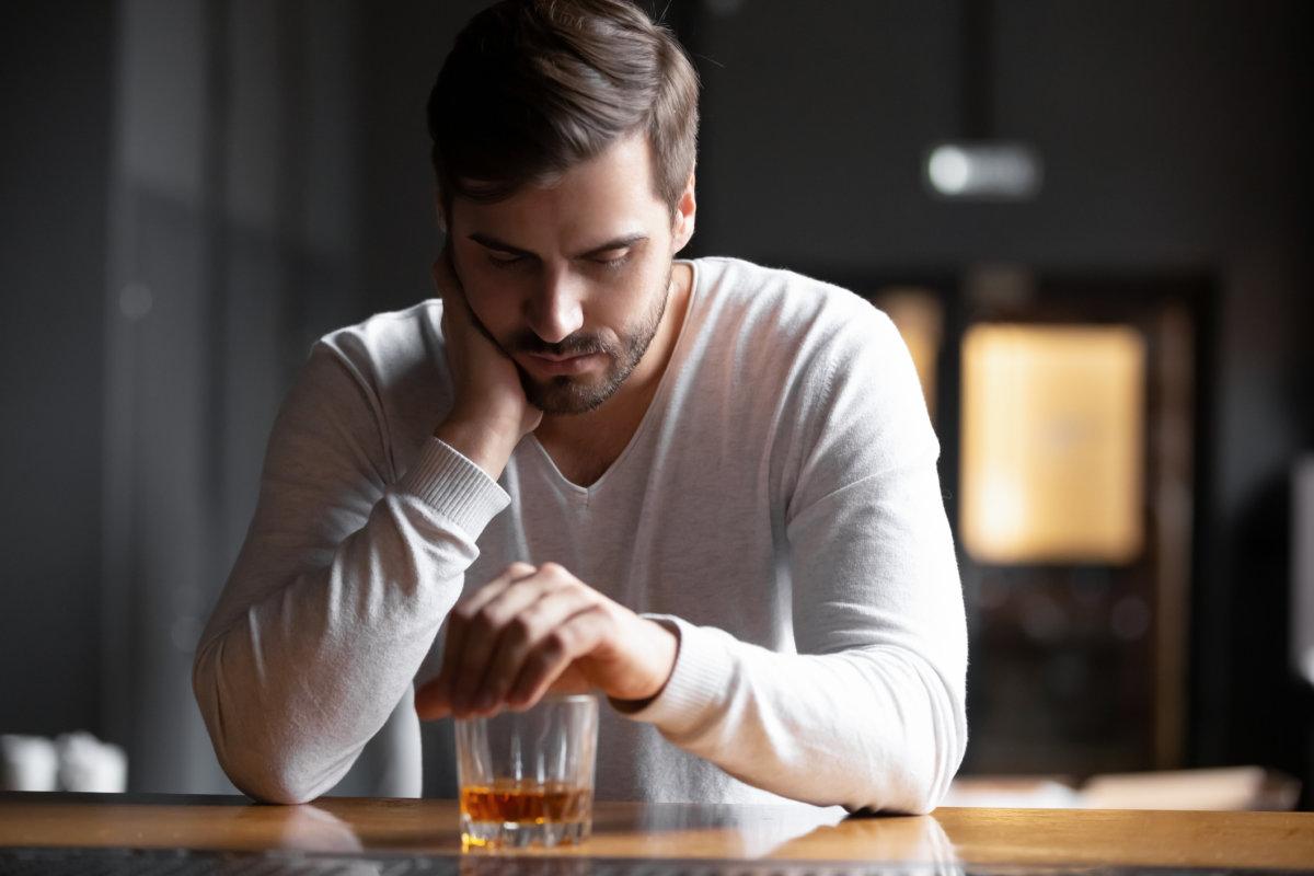 Verärgerter Mann, Trinker, Alkoholiker, sitzt mit einem Glas allein und trinkt Whiskey