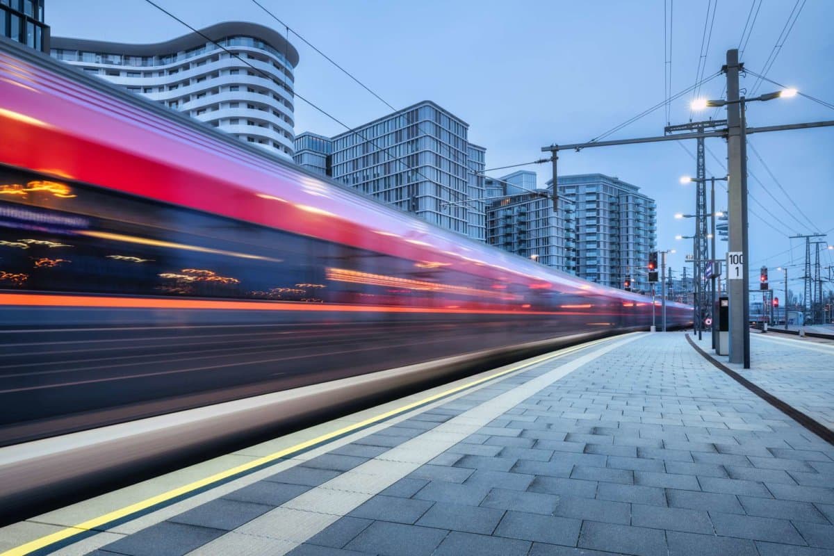 Hochgeschwindigkeitszug in Bewegung auf dem Bahnhof bei Sonnenuntergang. Bewegender roter moderner Intercity-Personenzug, Bahnsteig, Gebäude, Stadtlichter. Eisenbahn in Wien, Österreich. Eisenbahntransport