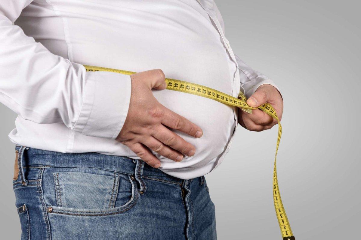 Übergewichtiger Mann misst seinen Bauch mit Maßband
