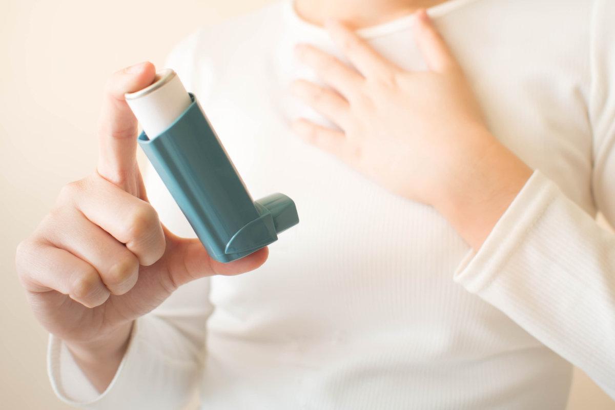 Young female in white t-shirt using blue asthma inhaler for reli