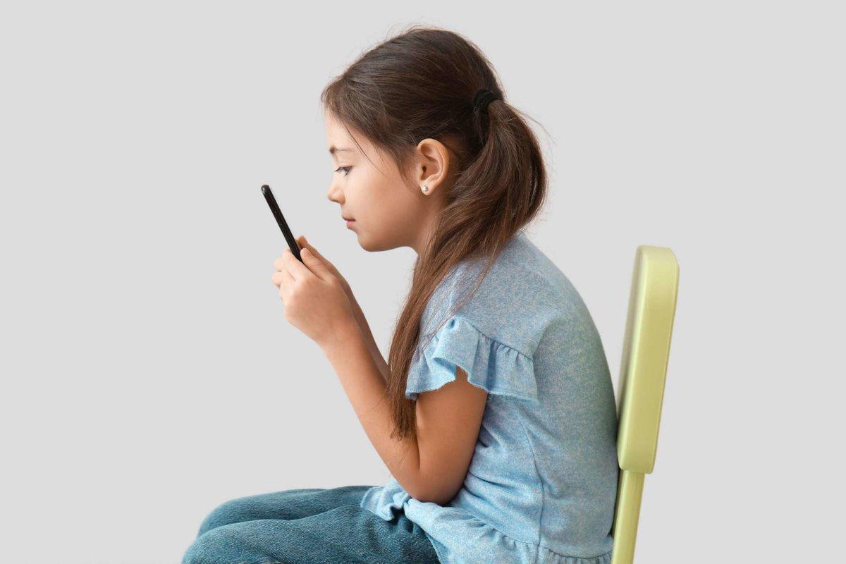 Little girl with bad posture using mobile phone on light background