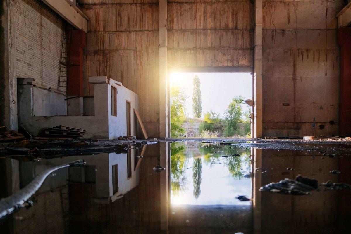 Inside of flooded dirty abandoned ruined industrial building with water reflection.
