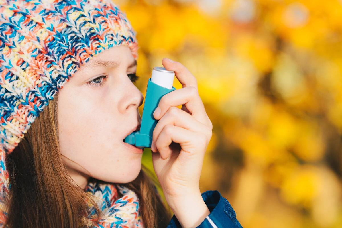 Asthma patient girl inhaling medication for treating shortness of breath and wheezing in a park