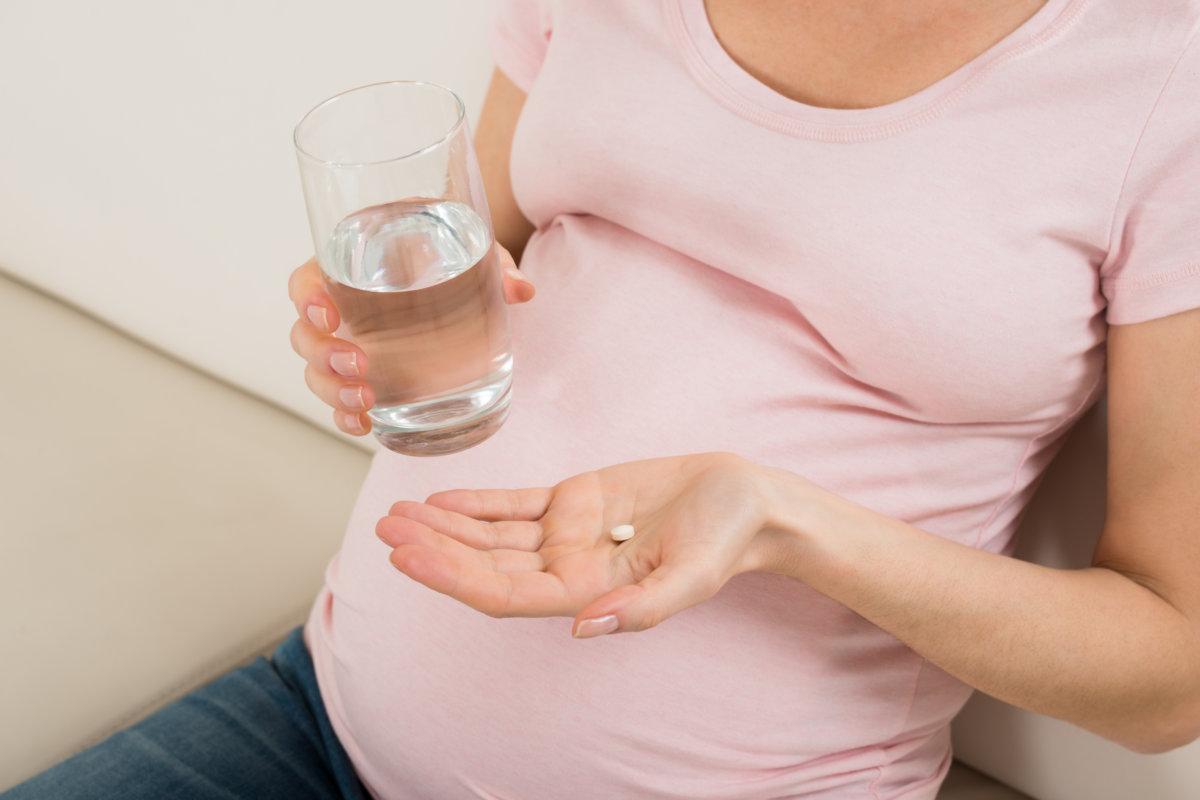 Close-up Of Pregnant Woman Hand With Glass Of Water And Vitamin Pill