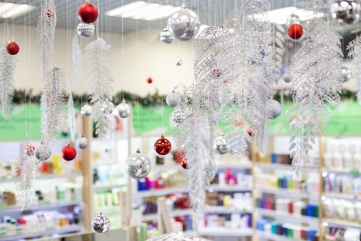 Christmas decorations: Christmas balls, tinsel branches in cosmetic shop. Blurred shelves with skin and hair care products in a cosmetic store as background