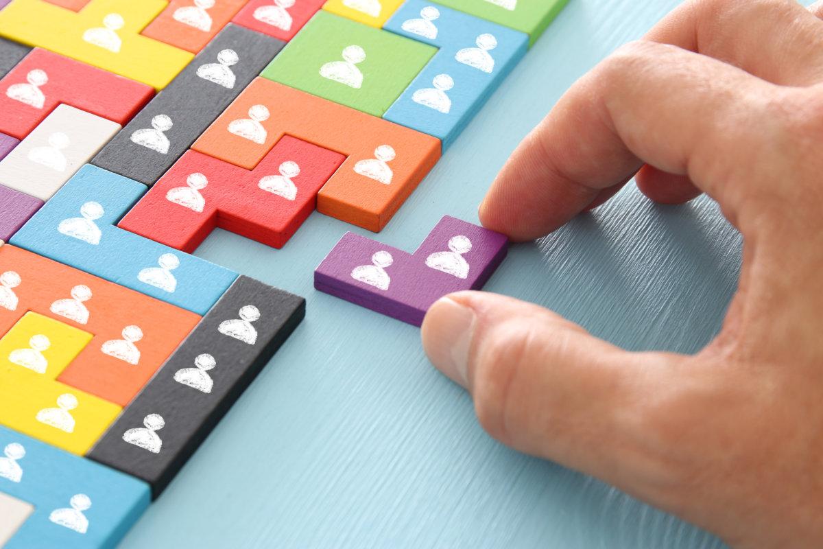 Bild von Tangram-Puzzleblöcken mit Personensymbolen über Holztisch, Personalwesen und Managementkonzept