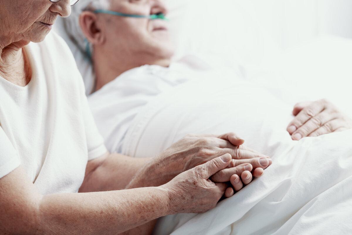 Älterer Mann mit Lungenkrebs liegt im Hospizbett und wird von seiner älteren Frau gestützt, Foto mit Kopierraum