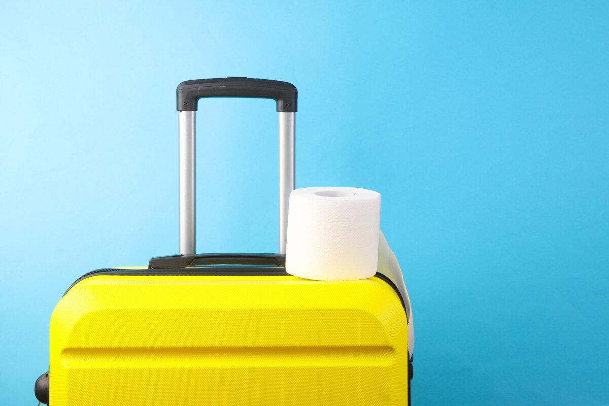 Gelber Plastikreisekoffer und Toilettenpapierrolle auf blauem Hintergrund. Tourismus, Urlaubskonzept