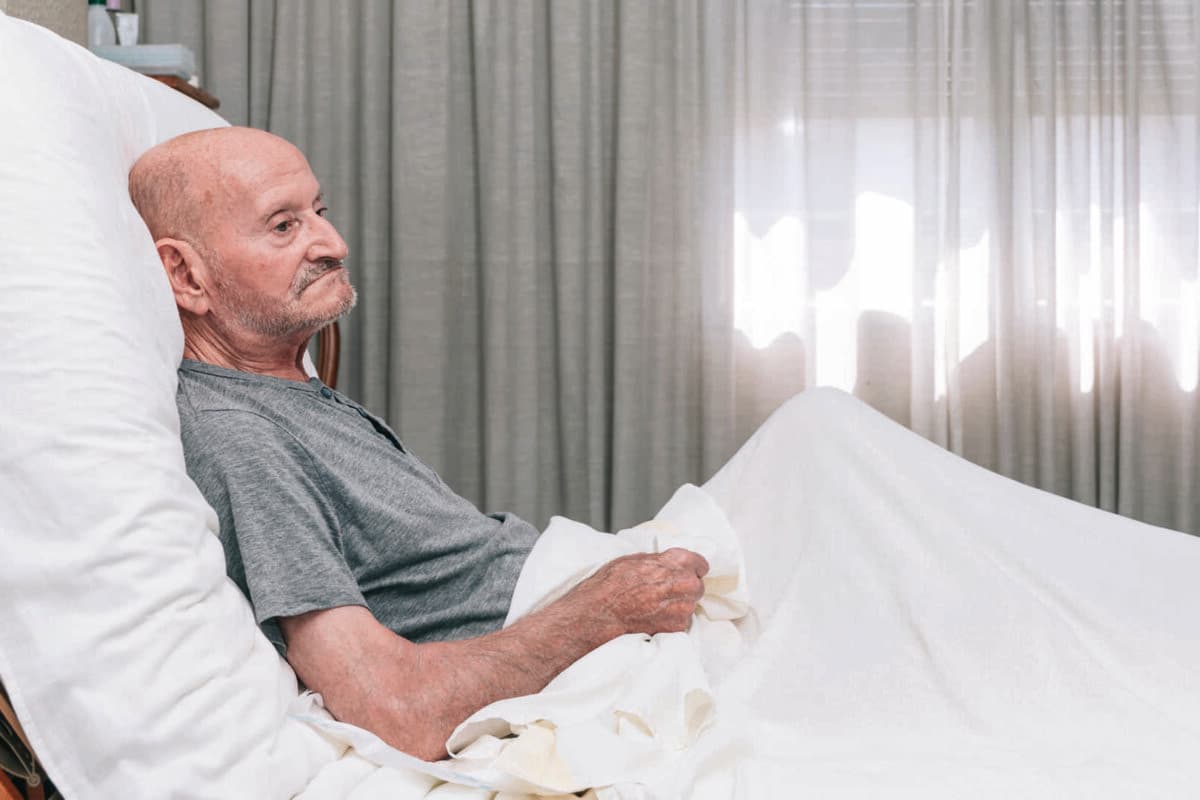 älterer Mann liegt allein auf einem Bett. Horizontal