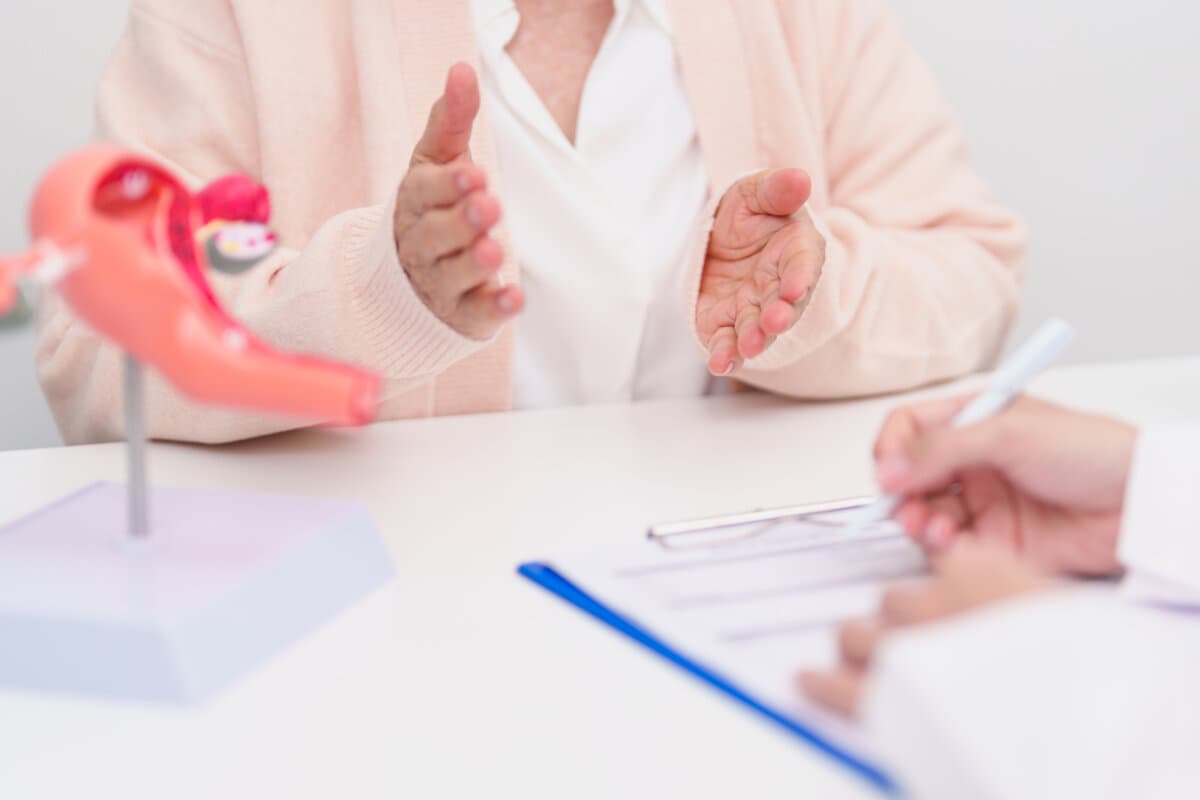 Ältere Patientin berät Arzt mit Anatomie der Gebärmutter und Eierstöcke.