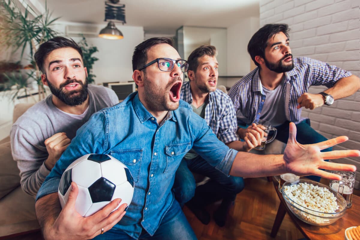 Men watching sport on tv together at home screaming cheerful.