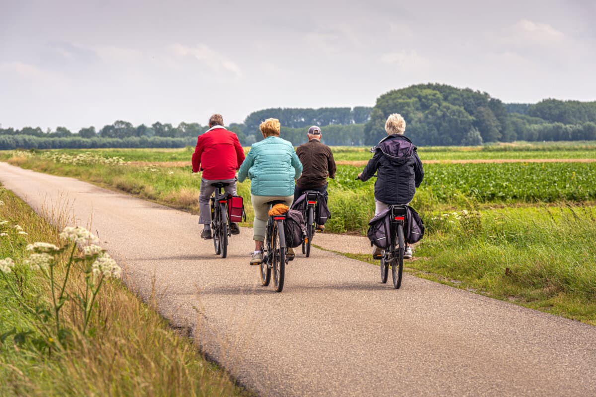 Two elderly unidentified couples with e-bikes cycle on a Dutch country road between fields in the province of North Brabant.